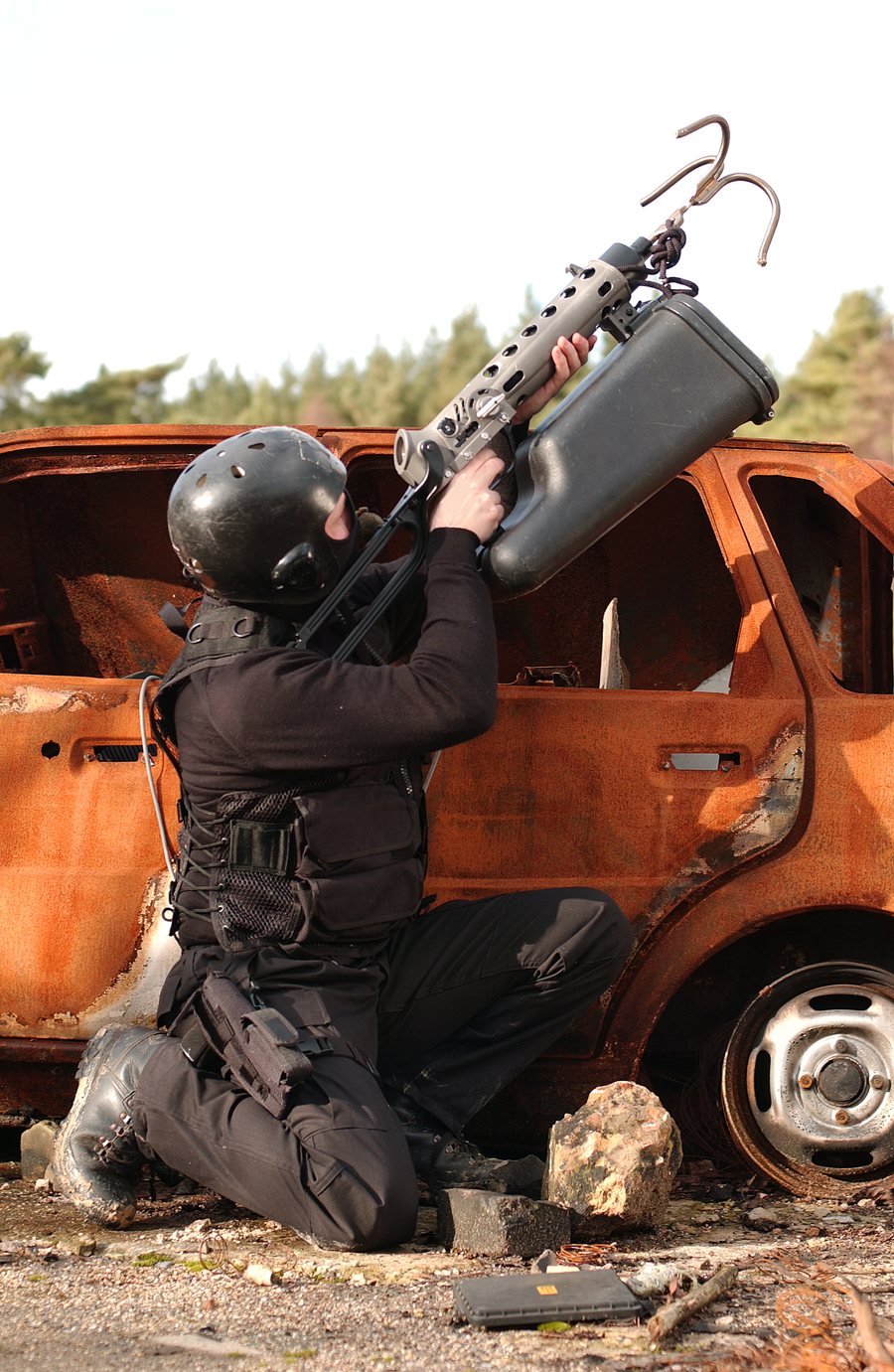 Operator kneeling by a vehicle, aiming an ALM grapnel launcher upward