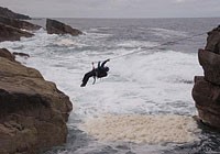 Soldier crossing a rope over rocky surf